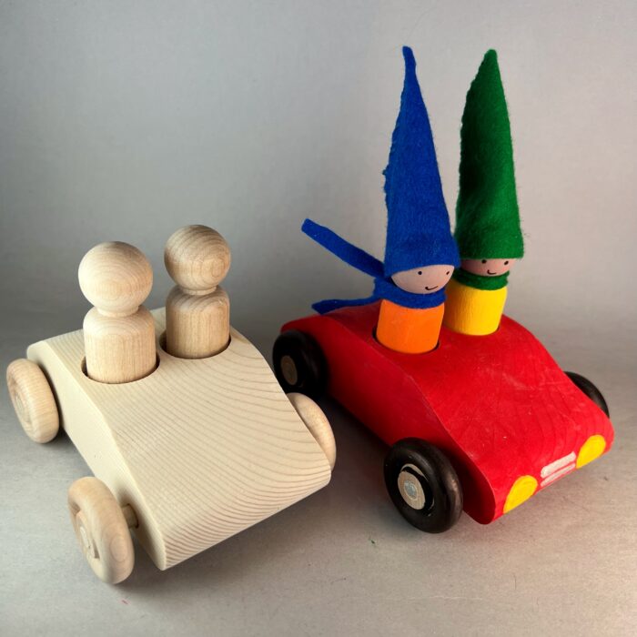 Gnome Mobile Kit. An unfinished two seater car with two wooden peg dolls is parked beside a painted two-seater car with two painted gnomes with tall hats and scarves in bright colors.