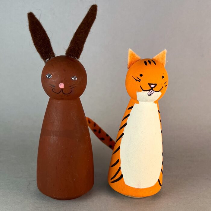 Wooden Peg Animals Kit. A brown painted wooden peg bunny, beside a white, orange, and black wooden peg cat.