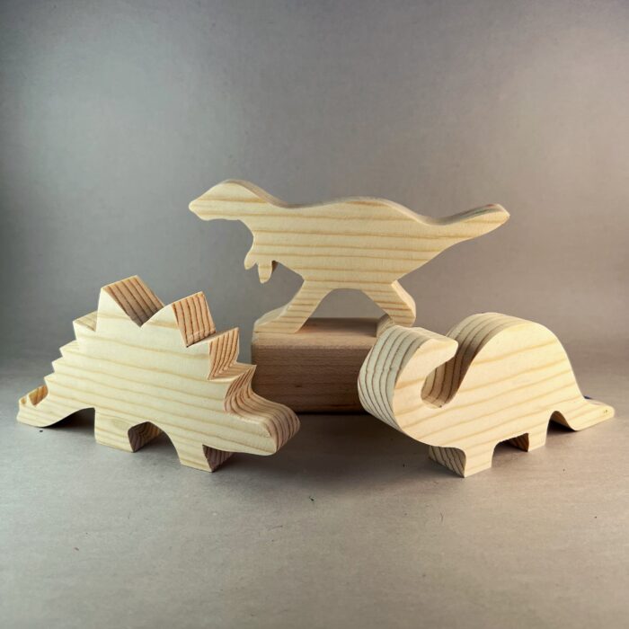 Watercolor Dinosaurs Kit. Three plain wood dinosaur shapes are standing in a group: T-Rex, Stegasuarus, and Brontosuarus..