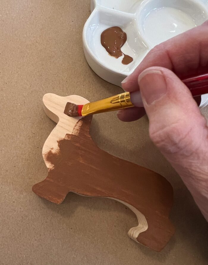 Painted Dogs Kit. A wood cutout of a dachshund, getting painted brown with a paint brush.
