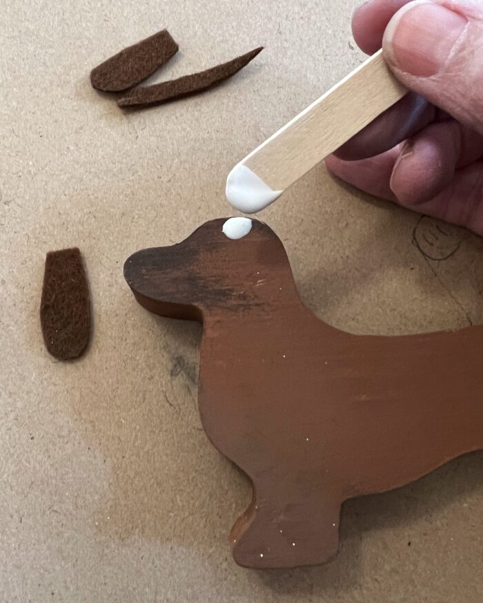 Painted Dogs Kit. Glue on a craft stick being applied to Dachsund's head, to attach ears.