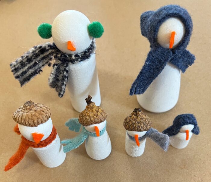Snow Family Kit. showing six wooden peg dolls, painted white nd dercorated with hats, scarves, and noses.